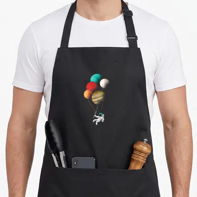 Tablier de cuisine noir avec un astronaute tenant des planètes colorées en forme de ballons.
