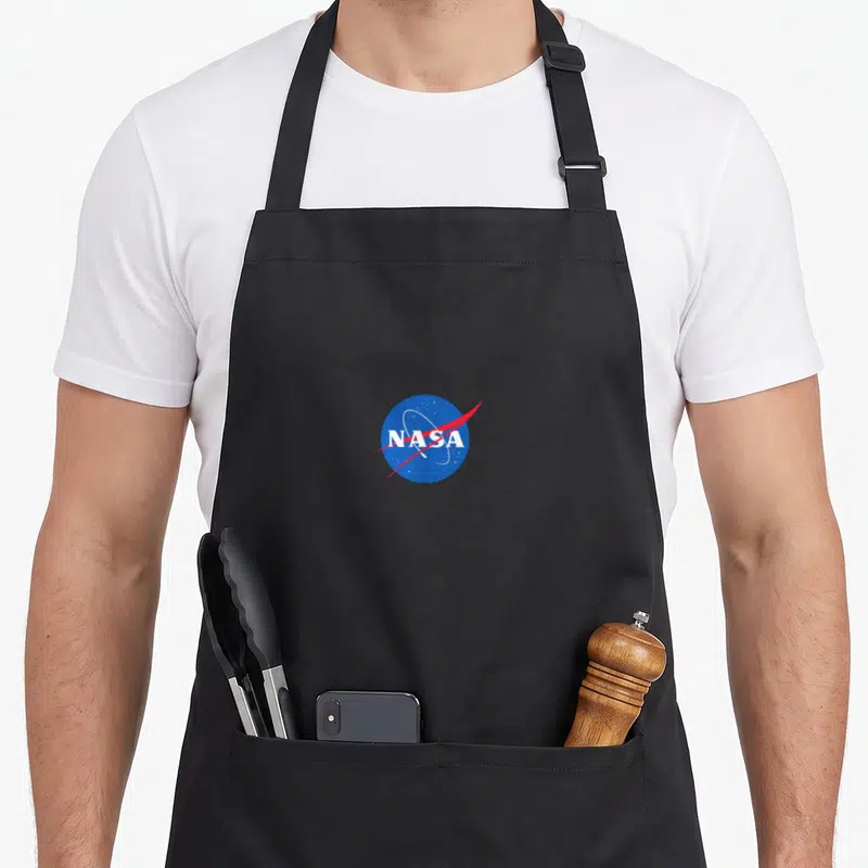 Tablier de cuisine noir avec le logo circulaire bleu et rouge NASA au centre du torse.