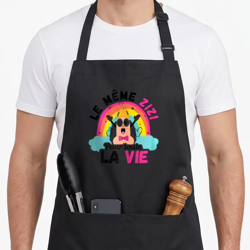 Tablier de cuisine noir avec un personnage rose devant un arc-en-ciel et le texte Le même Zizi pour toute la vie.