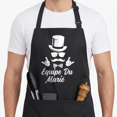 Tablier de cuisine noir avec Équipe Du Marié, chapeau haut de forme, moustache et gants en blanc.