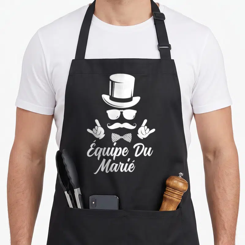 Tablier de cuisine noir avec Équipe Du Marié, chapeau haut de forme, moustache et gants en blanc.