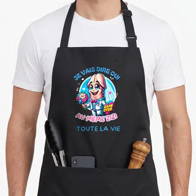 Tablier de cuisine noir avec illustration colorée d'un personnage en costume de marié tenant des fleurs et le texte Je vais dire oui.