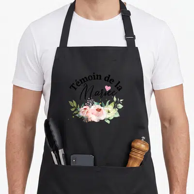 Tablier de cuisine noir avec inscription Témoin de la Mariée entouré de roses roses et blanches ainsi que de feuilles vertes.