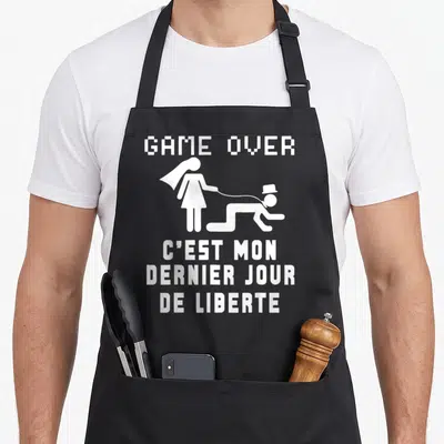 Tablier de cuisine noir avec une illustration blanche d'un homme menotté à sa future épouse sous le texte Game Over C'est mon dernier jour de liberte.