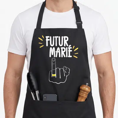 Tablier de cuisine noir avec poing levé portant une alliance et le texte Futur Marié en lettres blanches et jaunes.