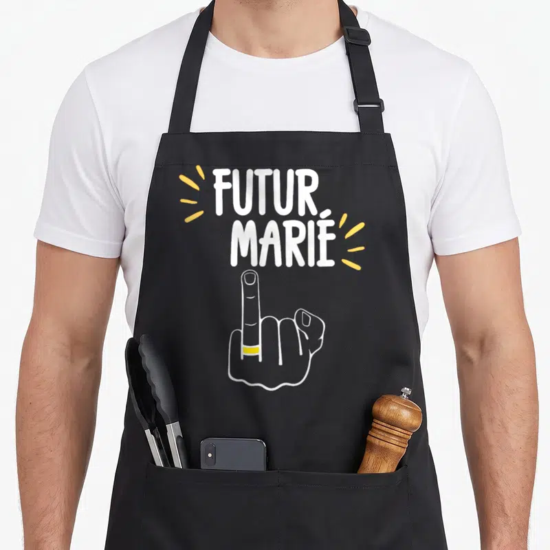 Tablier de cuisine noir avec poing levé portant une alliance et le texte Futur Marié en lettres blanches et jaunes.