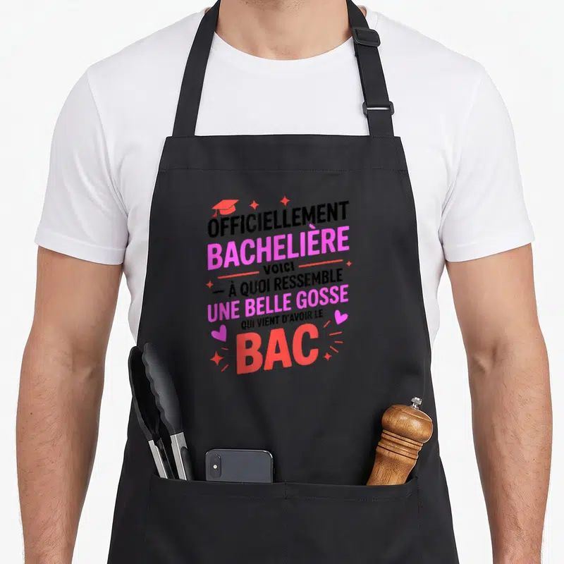 Tablier de cuisine noir avec inscription « Officiellement Bachelière » et illustration de toque de graduation rose et étoiles scintillantes.