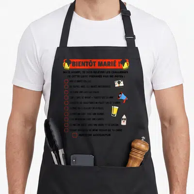 Tablier de cuisine noir avec liste de challenges humoristiques et bierres en illustration.