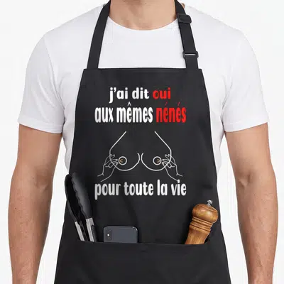 Tablier de cuisine noir avec texte blanc et rouge et illustration de seins stylisés en lignes fines.