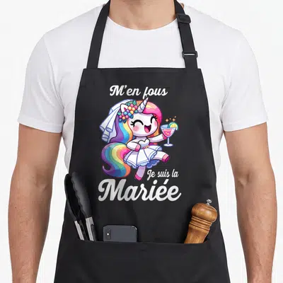 Tablier de cuisine noir avec une licorne rose en robe de mariée tenant un verre et le texte M'en fous Je suis la Mariée