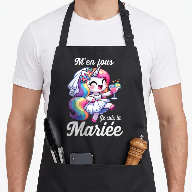 Tablier de cuisine noir avec une licorne rose en robe de mariée tenant un verre et le texte M'en fous Je suis la Mariée