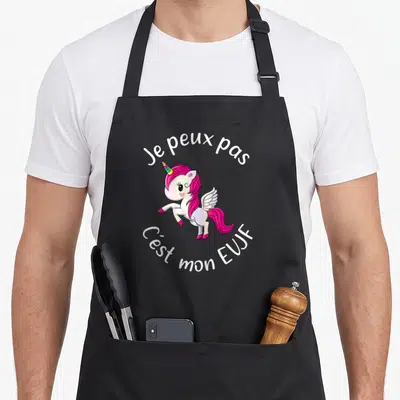 Tablier de cuisine noir avec une licorne rose ailée et le texte Je peux pas c'est mon EUJF imprimé en blanc.
