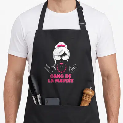 Tablier de cuisine noir avec illustration d'une femme coiffée d'une couronne et le texte Gang de la Mariée en rose vif.
