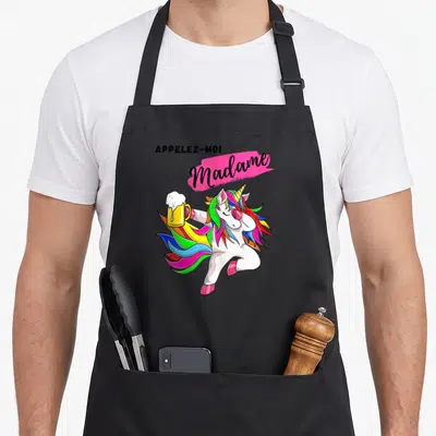 Tablier de cuisine noir avec illustration d'une licorne colorée tenant une bière et le texte Appelez-moi Madame sur fond rose vif.