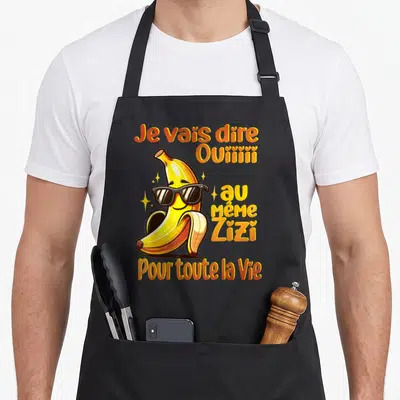 Tablier de cuisine noir avec une banane animée portant des lunettes noires et du texte humoristique jaune et orange.