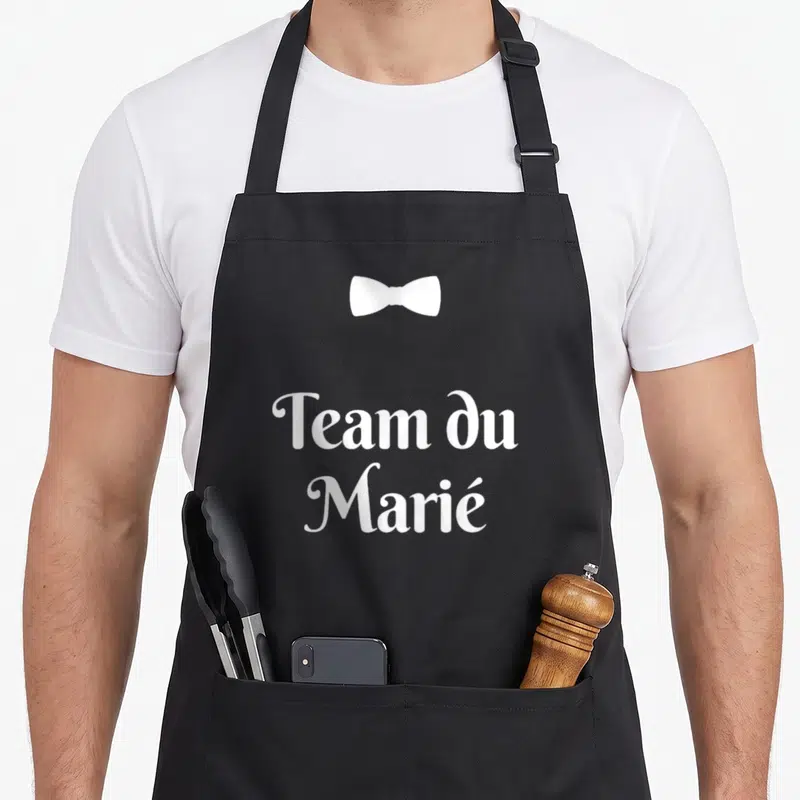 Tablier de cuisine noir avec inscription Team du Marié et un nœud papillon blanc stylisé.