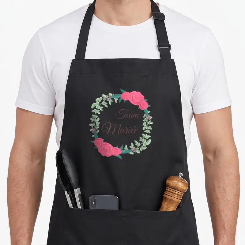 Tablier de cuisine noir avec une couronne de roses roses et le texte Team Mariée au centre.