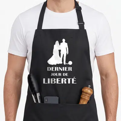 Tablier de cuisine noir avec silhouette blanche couple et texte dernier jour de liberté imprimé en blanc.