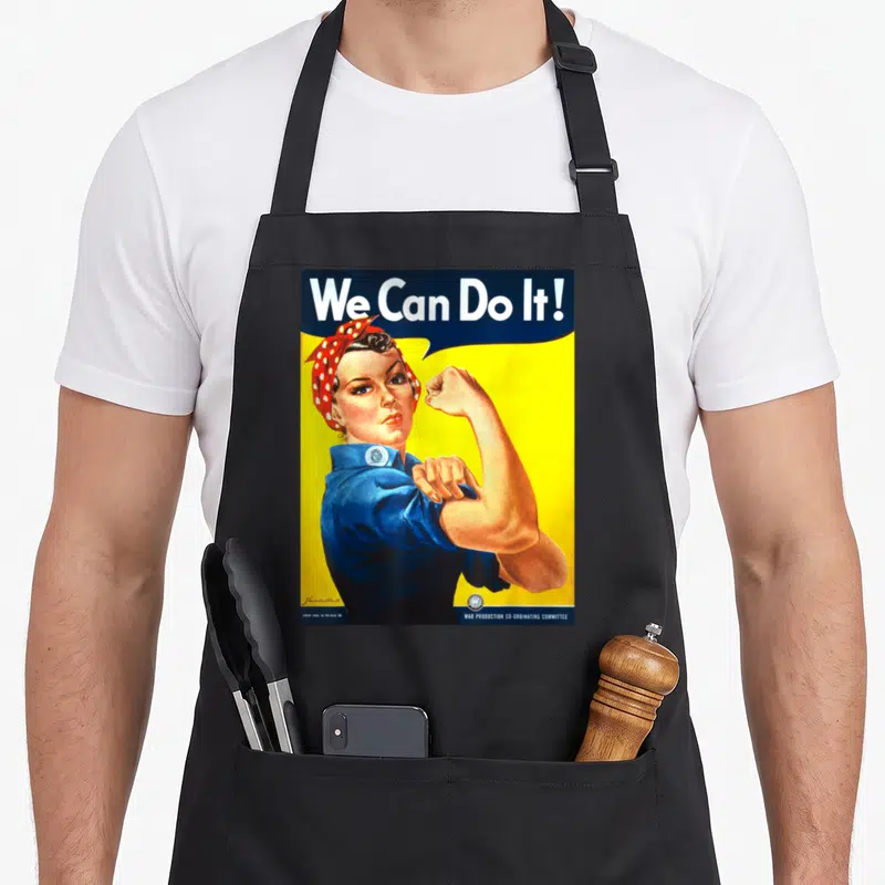 Tablier de cuisine noir avec l'illustration colorée de Rosie The Riveter et le texte We Can Do It en haut.
