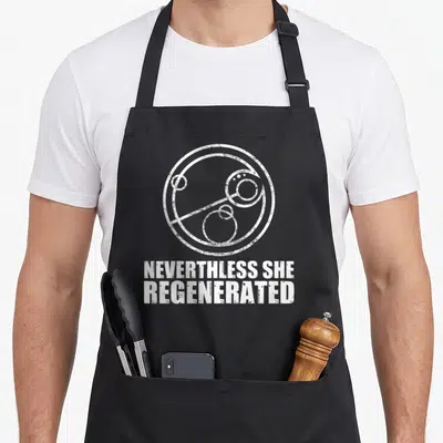 Tablier de cuisine noir avec inscription Nevertheless She Regenerated et symbole circulaire blanc stylisé.