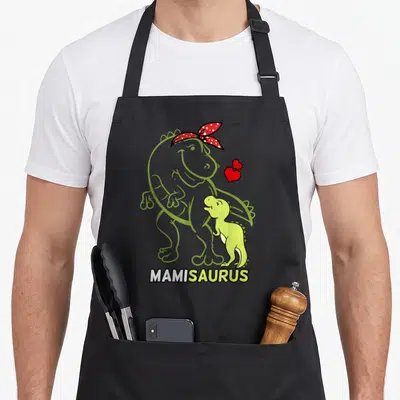 Tablier de cuisine noir avec dinosaure vert, contour mamie et texte MAMISAURUS en bas.