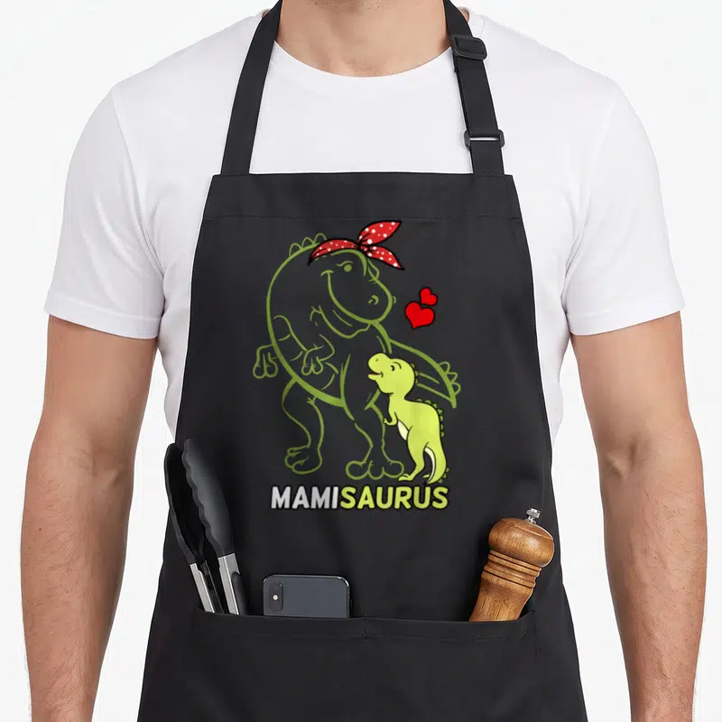 Tablier de cuisine noir avec dinosaure vert, contour mamie et texte MAMISAURUS en bas.