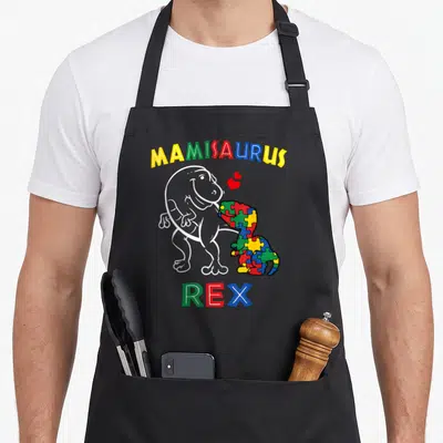Tablier de cuisine noir avec un dinosaure blanc et un dinosaure en puzzle coloré sous le texte Mamisaurus Rex.