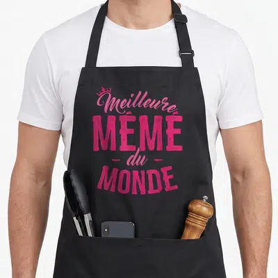 Tablier de cuisine noir avec l'inscription Meilleure Mémé du Monde en rose vif surplombée d'une petite couronne.