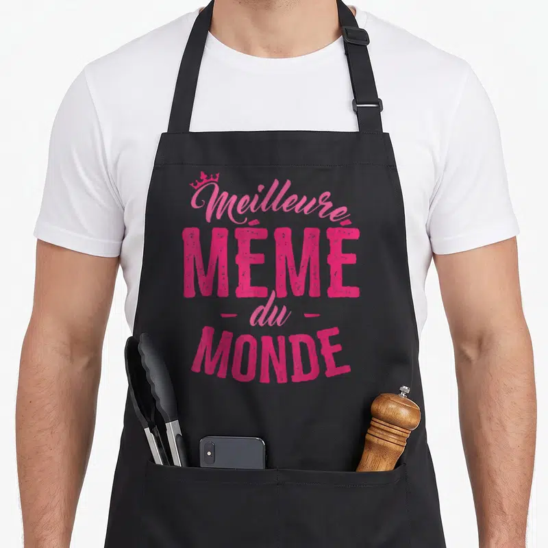 Tablier de cuisine noir avec l'inscription Meilleure Mémé du Monde en rose vif surplombée d'une petite couronne.