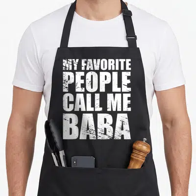 Tablier de cuisine noir avec le texte MY FAVORITE GENS CALL ME BABA en lettres blanches capitales.