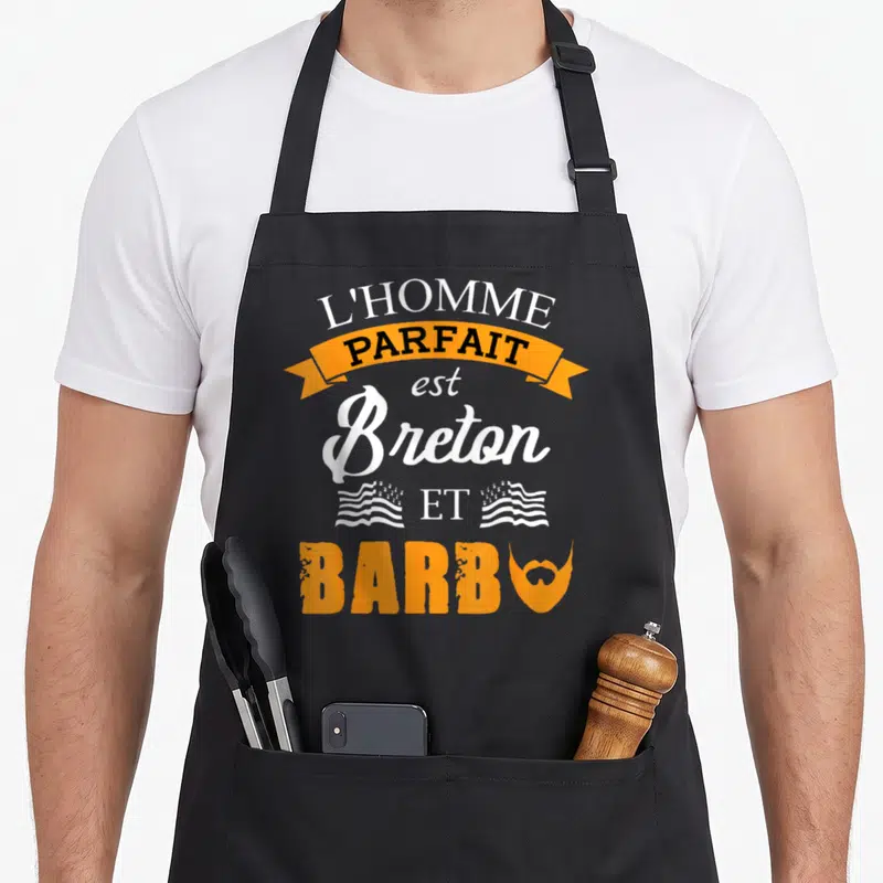 Tablier de cuisine noir avec inscription L'homme parfait est Breton et Barbu en orange et blanc.