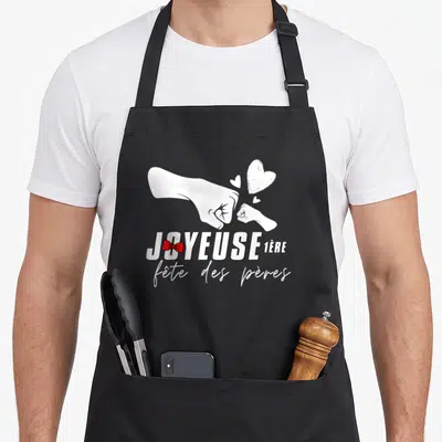 Tablier de cuisine noir avec inscription Joyeuse 1ère fête des pères et illustration de deux poings se touchant.