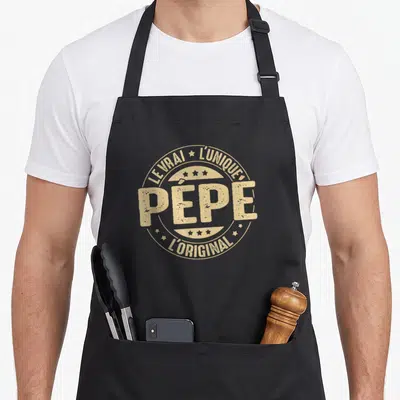 Tablier de cuisine noir avec un logo circulaire doré indiquant Pépe le vrai l'unique l'original entouré d'étoiles.