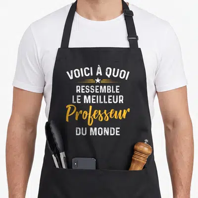 Tablier de cuisine noir avec inscription voici à quoi ressemble le meilleur professeur du monde en blanc et orange.