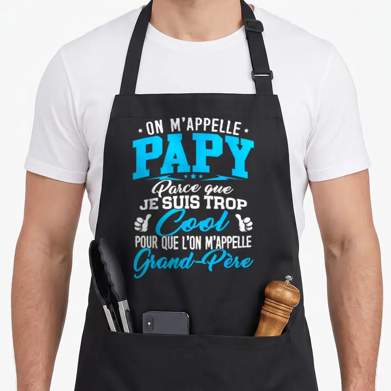 Tablier de cuisine noir avec inscription On m'appelle Papy parce que je suis trop cool pour que l'on m'appelle Grand-Père en bleu et blanc.