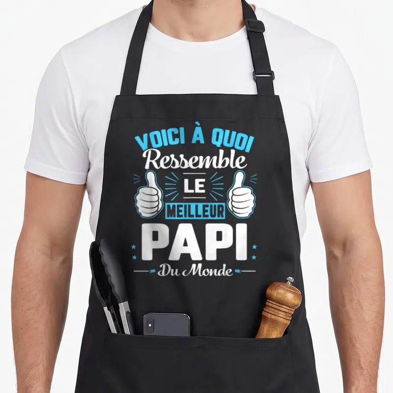 Tablier de cuisine noir avec inscription Voici à quoi Ressemble le Meilleur Papi Du Monde et deux pouces levés bleus et blancs.
