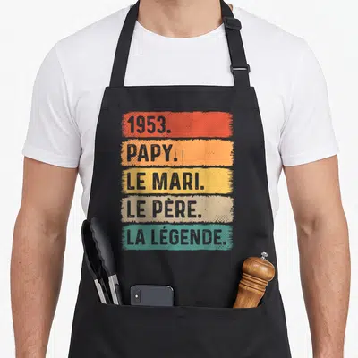 Tablier de cuisine noir avec inscription 1953 Papy Le Mari Le Père La Légende sur bandes colorées style vintage.