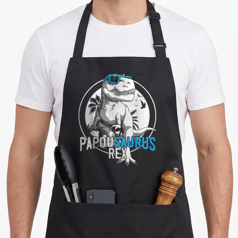 Tablier de cuisine noir avec un dinosaure T-Rex portant des lunettes bleues et le texte Papousaurus Rex.