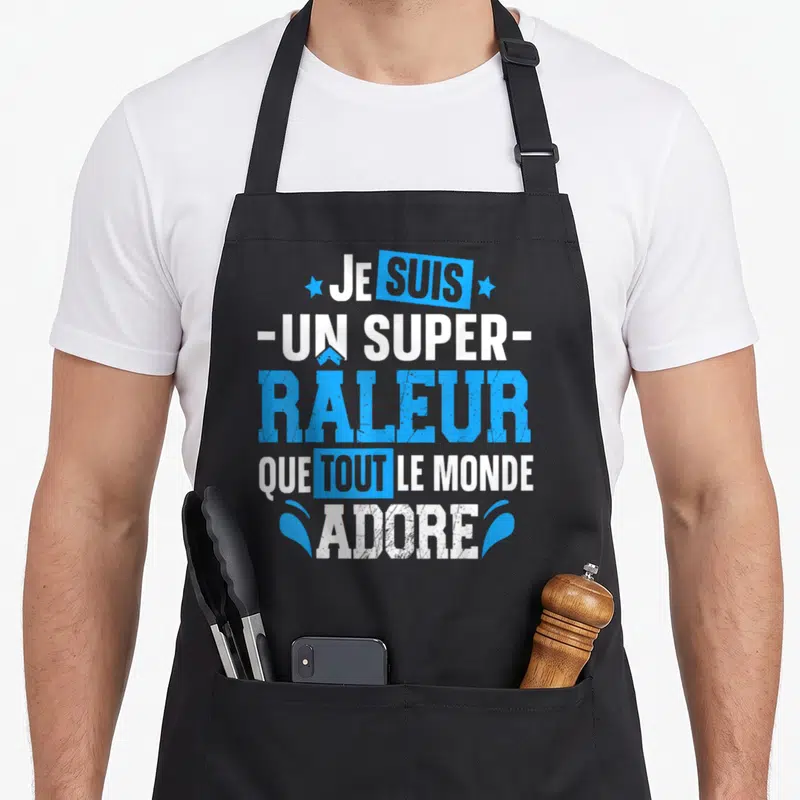 Tablier de cuisine noir avec l'inscription Je suis un super râleur que tout le monde adore en bleu et blanc.