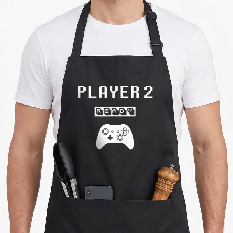 Tablier de cuisine noir avec texte Player 2 Ready et icône manette de jeu blanche en pixel art.