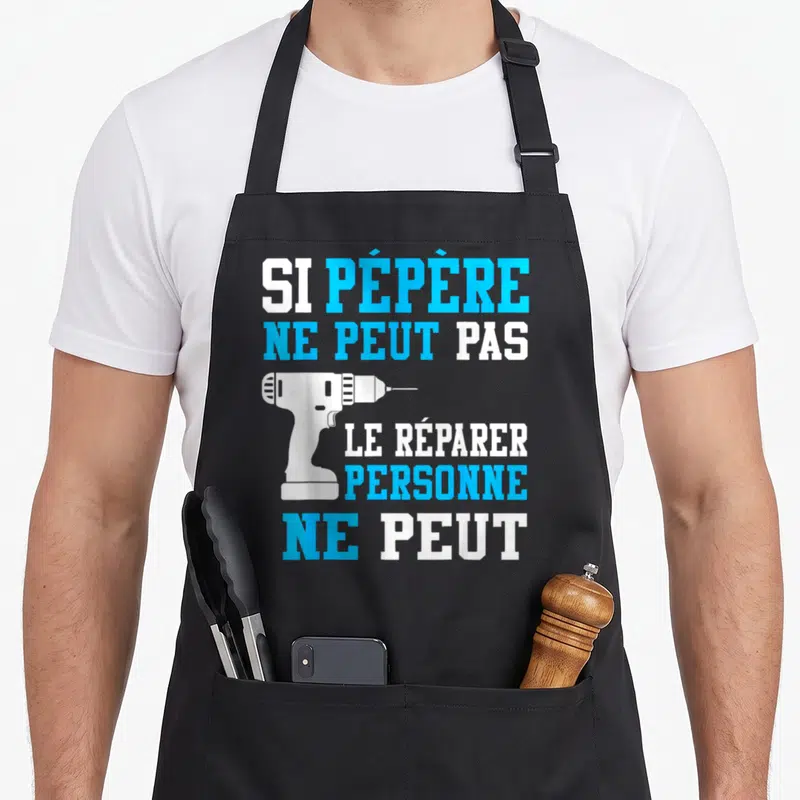 Tablier de cuisine noir avec texte blanc et bleu Si Pépère ne peut pas le réparer personne ne peut et une perceuse blanche.