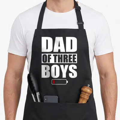 Tablier de cuisine noir avec inscription Dad of Three Boys et icône batterie rouge en bas.