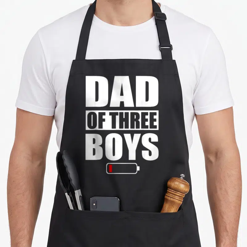 Tablier de cuisine noir avec inscription Dad of Three Boys et icône batterie rouge en bas.