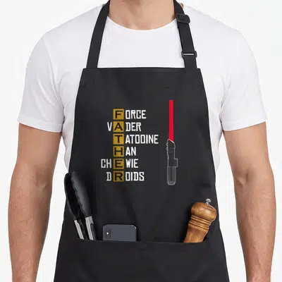 Tablier de cuisine noir avec acronymes Force Vader Tatooine Chewie Droids et sabre laser rouge.