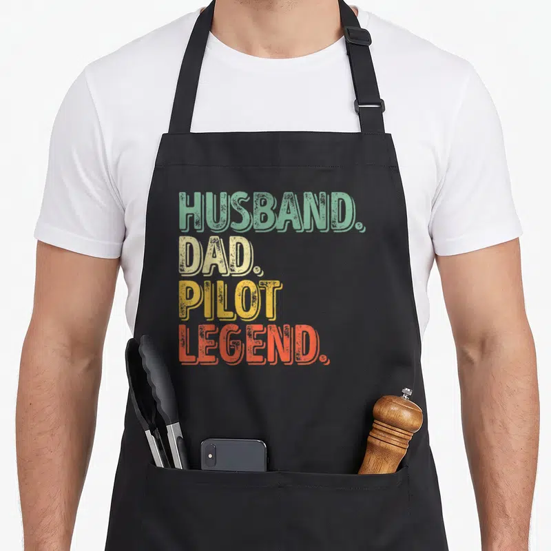 Tablier de cuisine noir avec le texte Husband Dad Pilot Legend en lettres colorées vintage.