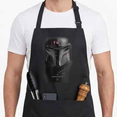 Tablier de cuisine noir avec le casque du Mandalorian et le logo de la série imprimés en gris et blanc.