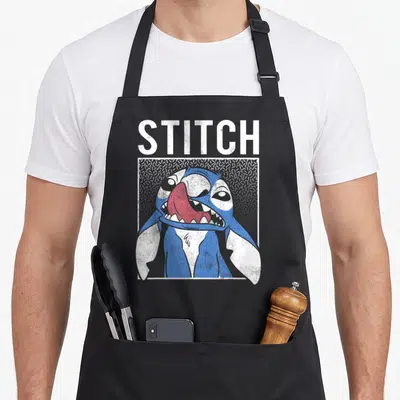 Tablier de cuisine noir avec illustration bleue de Stitch souriant dans un cadre blanc et texte STITCH au-dessus.
