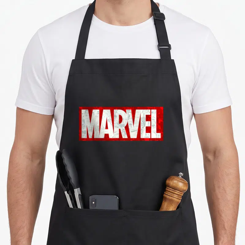 Tablier de cuisine noir avec un grand logo Marvel rouge contenant des dessins de comics en blanc dans les lettres.