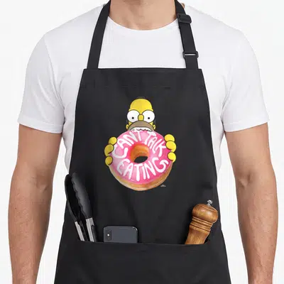 Tablier de cuisine noir avec Homer Simpson tenant un beignet rose portant l'inscription I CAN'T TALK EATING en blanc.