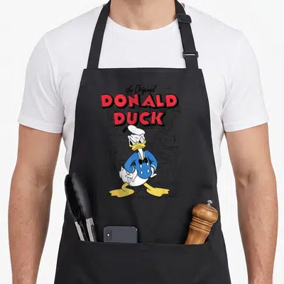 Tablier de cuisine noir avec illustration colorée de Donald Duck et notes de dessin technique en arrière-plan.